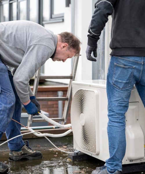 Two technicians installing an airconditioning unit outside a modern home.